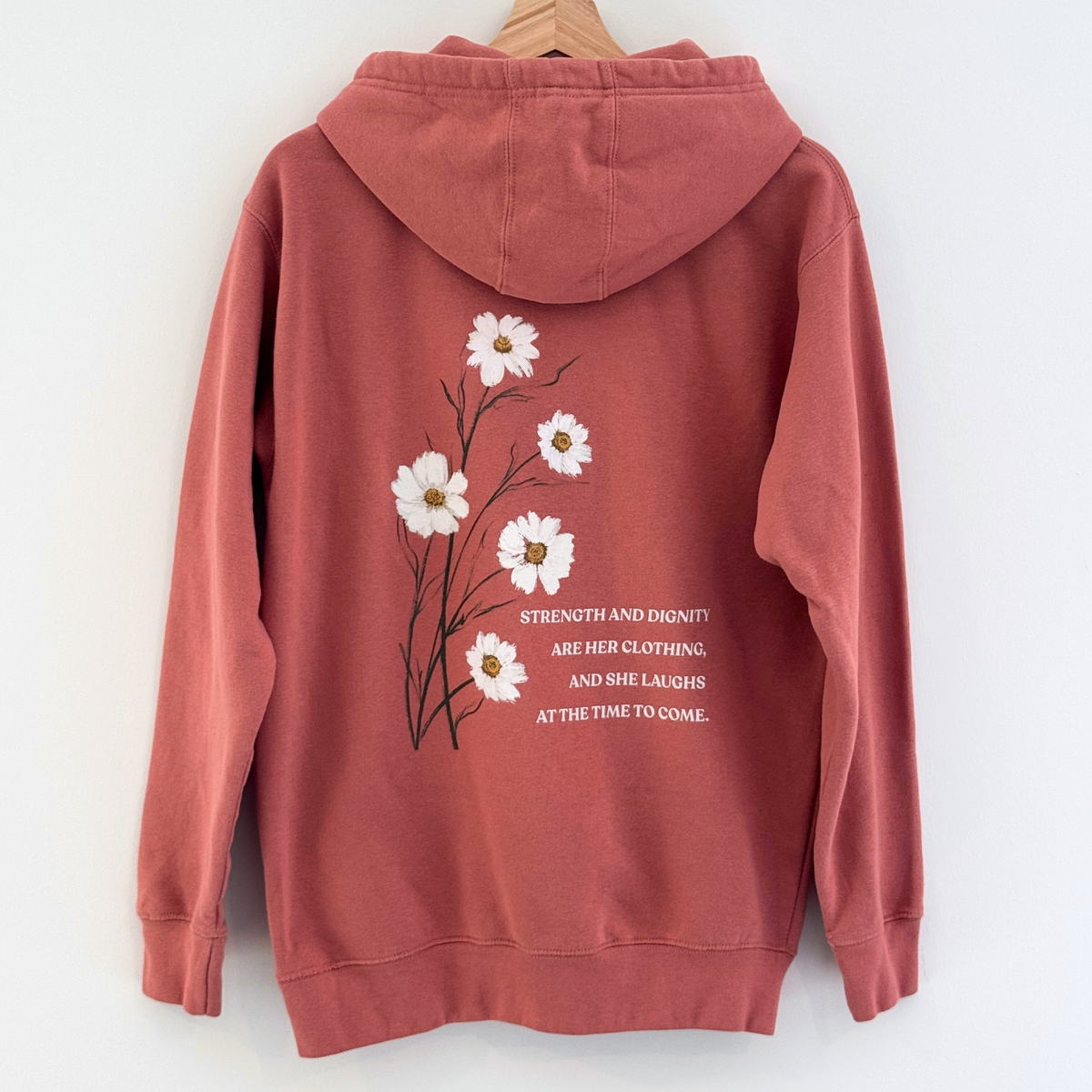Back of Dusty Rose hoodie with floral design and text of verse Proverbs 31:25 on a white background