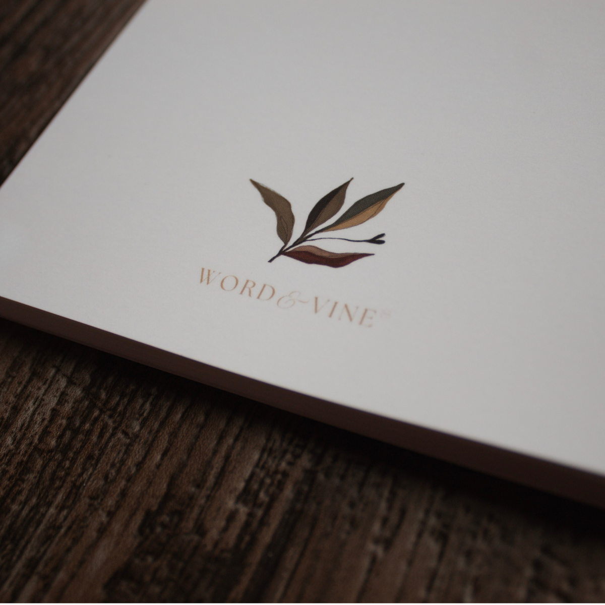 A close-up of the bullet journal's back cover resting on a dark wood surface. Features a logo of leaves and the brand name 'WORD and VINE'.