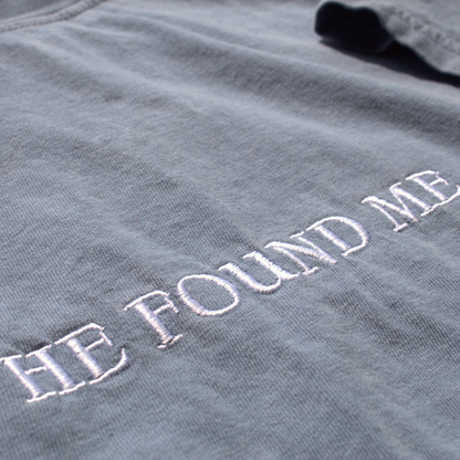close up of the Dusty blue tee with 'HE FOUND ME' embroidered in white thread