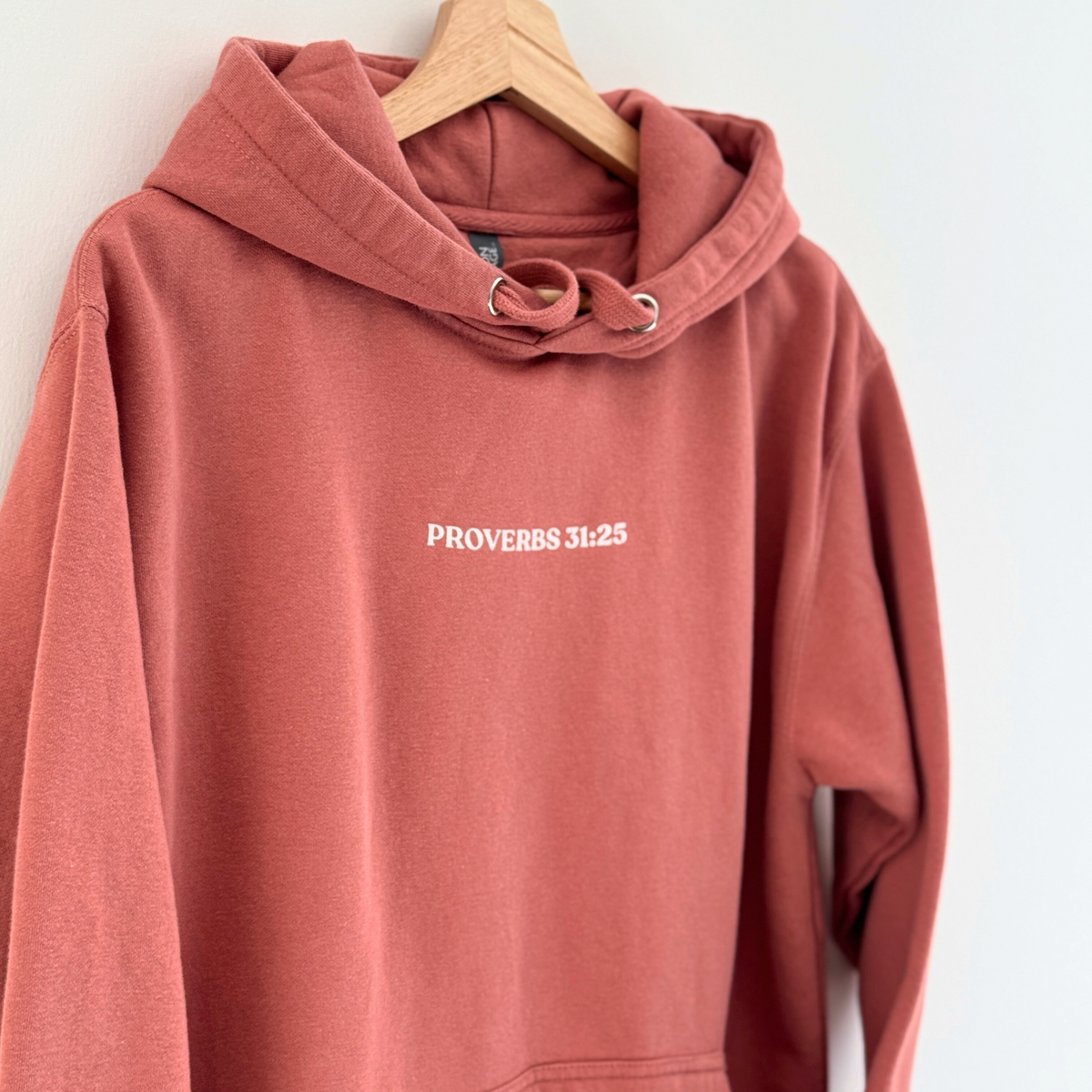 Front of Dusty Rose colored hoodie with 'Proverbs 31:25' text on a white background