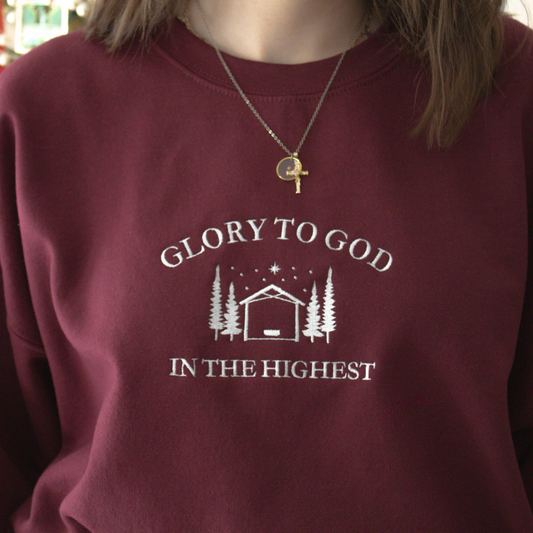 Maroon sweatshirt with Embroidered 'Glory to God in the Highest' text and simple manger and stable in between trees with stars and the star of David above.