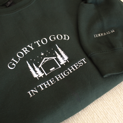 Forest Green sweatshirt with embroidered 'Glory to God in the Highest' text and simple manger and stable in between trees with stars and the star of David above. Sweatshirt sleeve features 'Luke 2:12-14' white embroidered text 