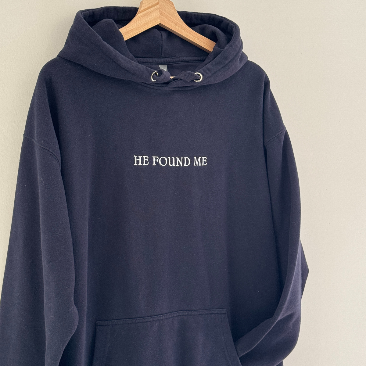Navy blue hoodie with embroidered 'HE FOUND ME' text on a white background