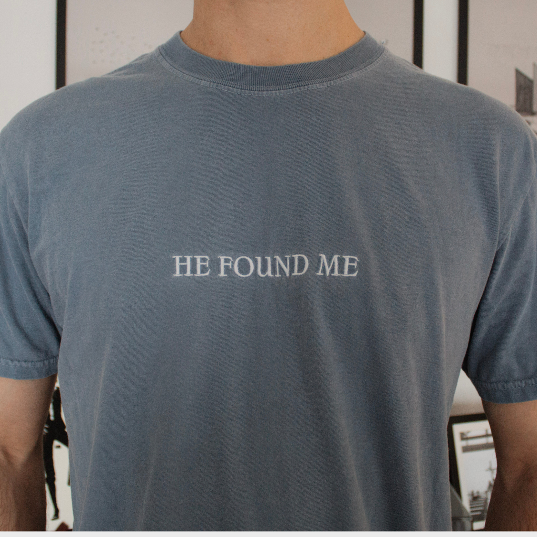 Person wearing a blue t-shirt with White Embroidered 'HE FOUND ME' text.