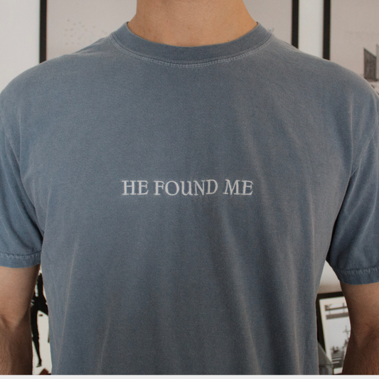 Person wearing a blue t-shirt with White Embroidered 'HE FOUND ME' text.