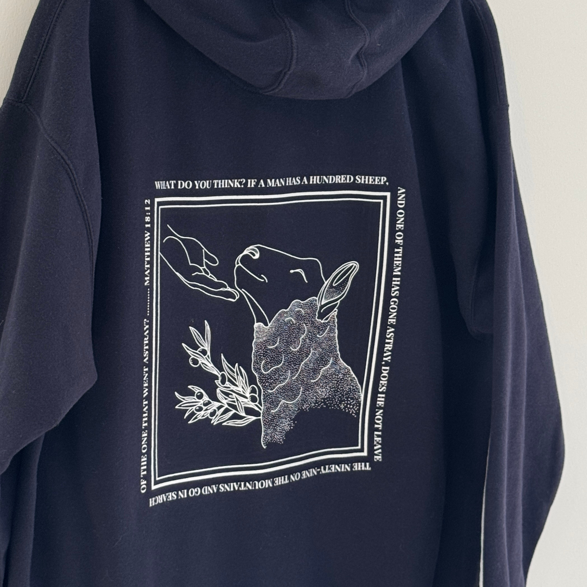 Closer look at Navy blue hoodie with white graphic line drawing of sheep being found and comforted by the hand of Jesus 