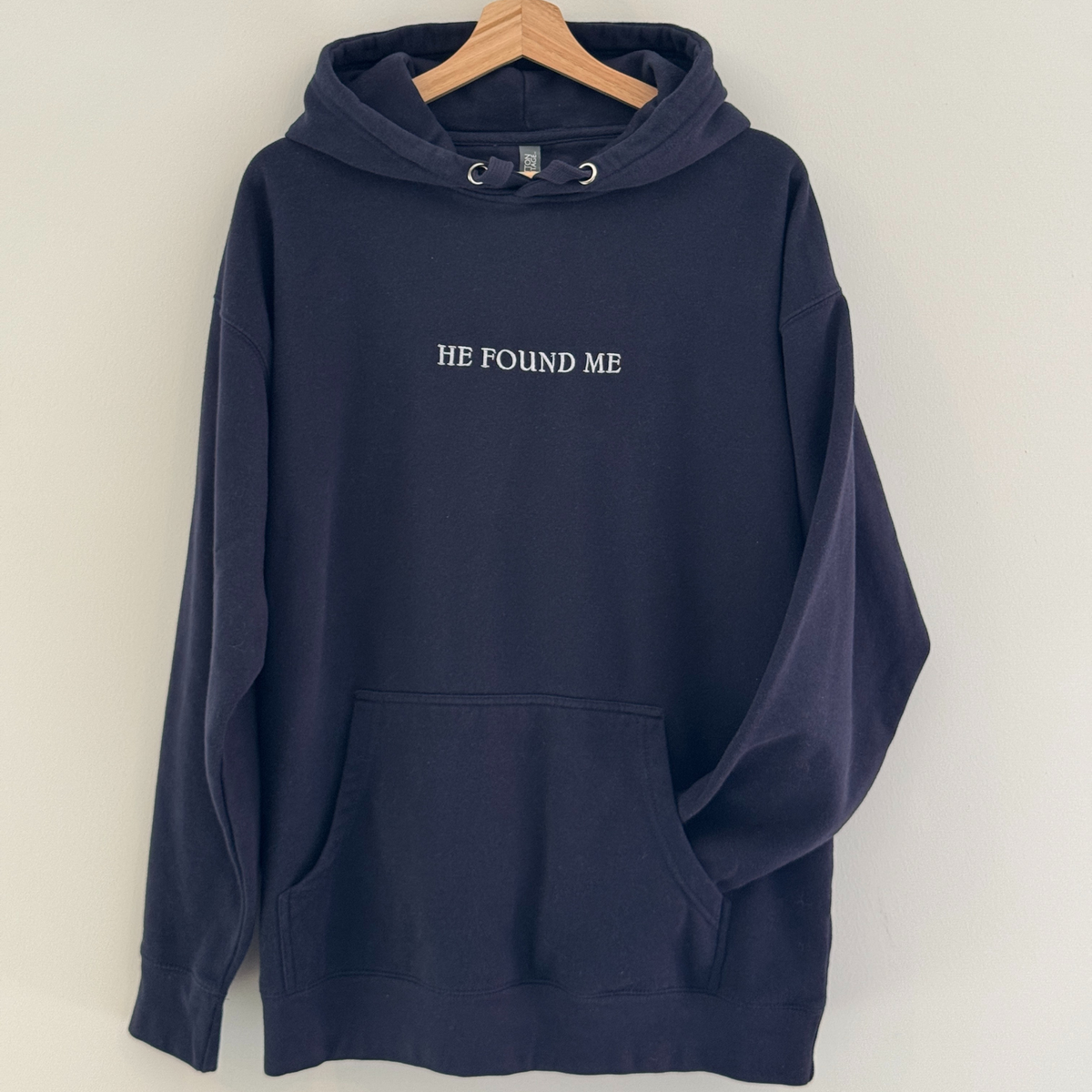 Navy blue hoodie with embroidered 'HE FOUND ME' text on a white background
