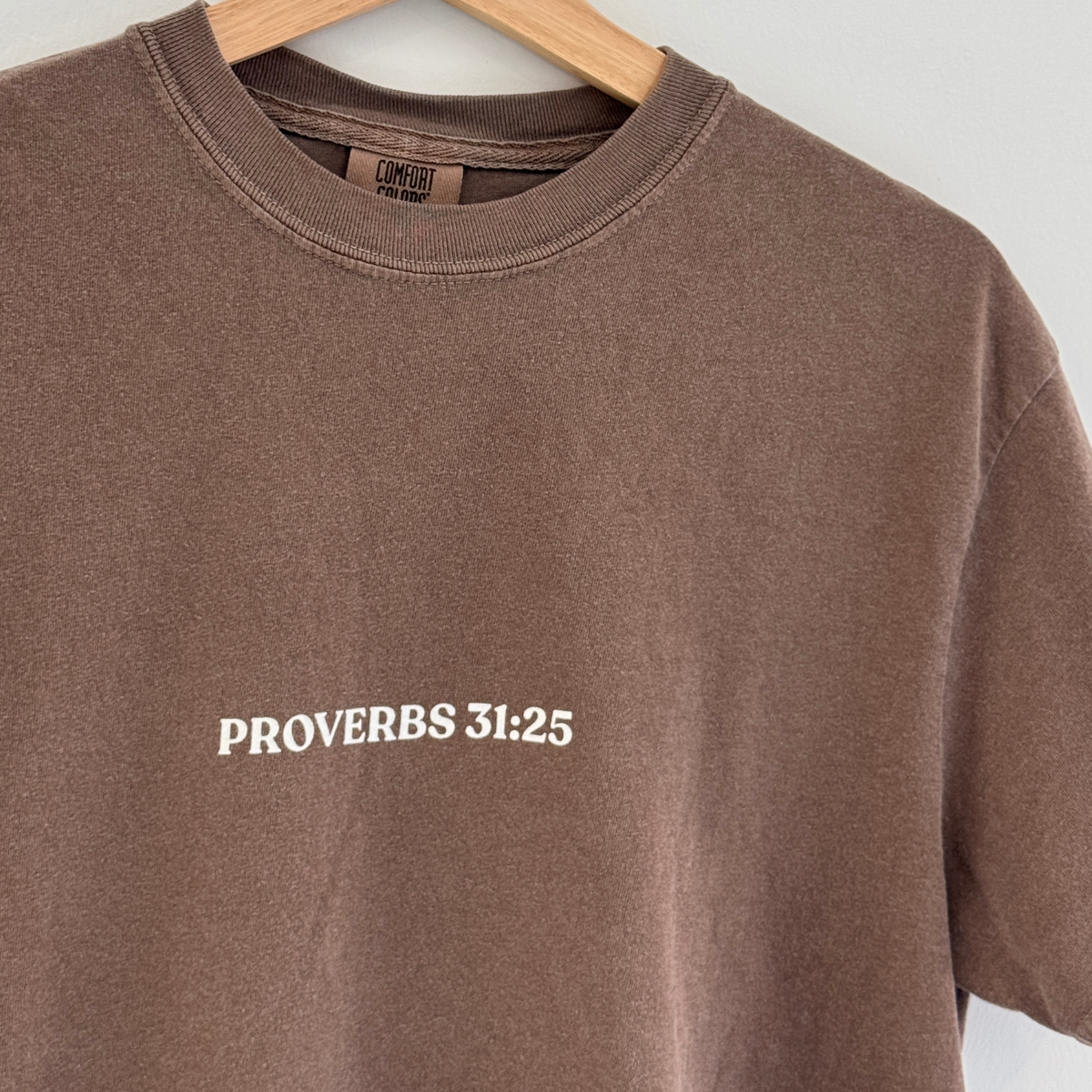 Brown t-shirt with 'Proverbs 31:25' text on a hanger