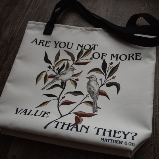 Product image taken at an angle: A white canvas tote bag with black handles, featuring a printed design of two birds on a leafy branch with the text 'ARE YOU NOT OF MORE VALUE THAN THEY? MATTHEW 6:26'.
