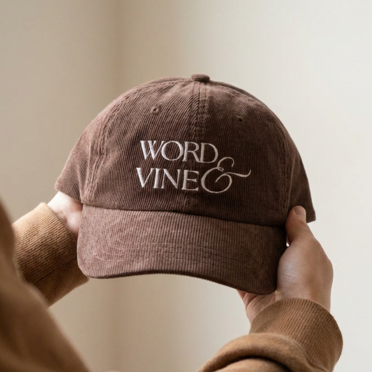 front of the Brown corduroy ball cap with 'WORD & VINE' embroidered held by a person against a neutral background