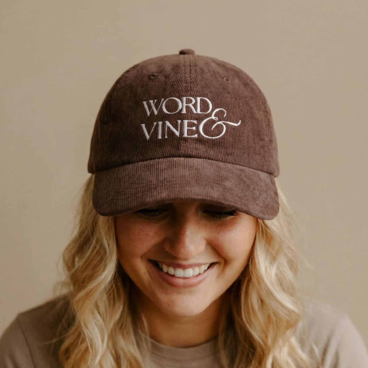 A Person wearing the brown corduroy ball cap with 'WORD & VINE' logo embroidered with white thread. 