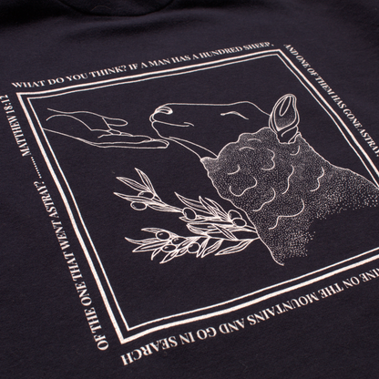 close up of navy blue hoodie with white line  graphic of a sheep being comforted by the hand of Jesus and text from Matthew 18:12