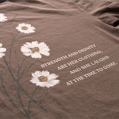 A close up of the back of the Brown t-shirt with white flowers and text reading 'strength and dignity are her clothing, and she laughs at the time to come. 